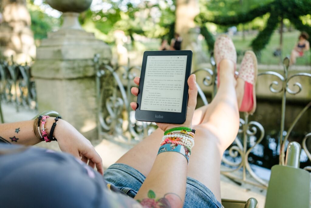 mujer sentada con sus piernas reposadas en el espaldar de una silla en alto, leyendo un ebook en su ipad.